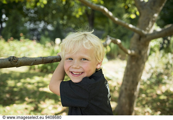 Portrait of smiling little boy blimbing on a tree