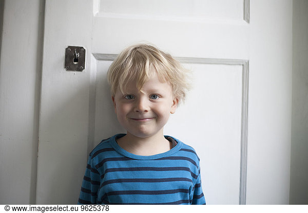 Portrait of smiling little boy in front of white door