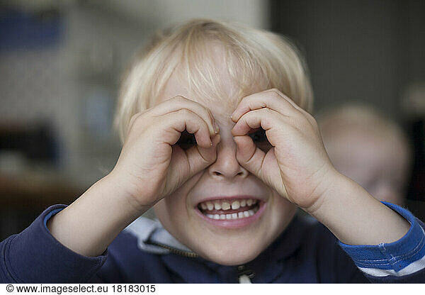 Portrait of smiling little boy looking through his hands formed like spectacles