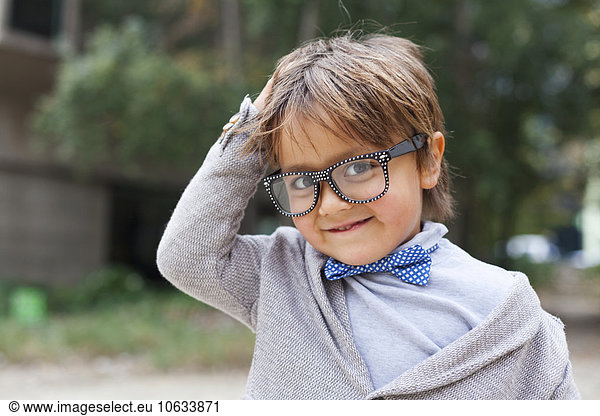 Portrait of smiling little boy with hand on his head wearing bow tie and oversized spectacles