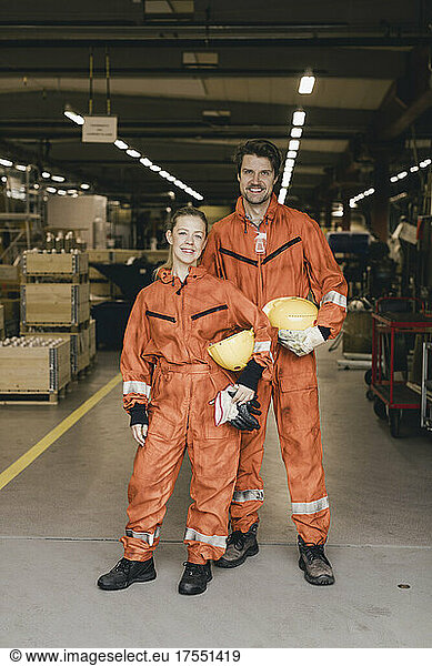 Portrait of smiling male and female coworkers in uniform standing at factory warehouse