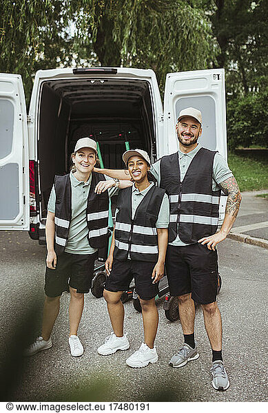 Portrait of smiling male and female coworkers standing against delivery van