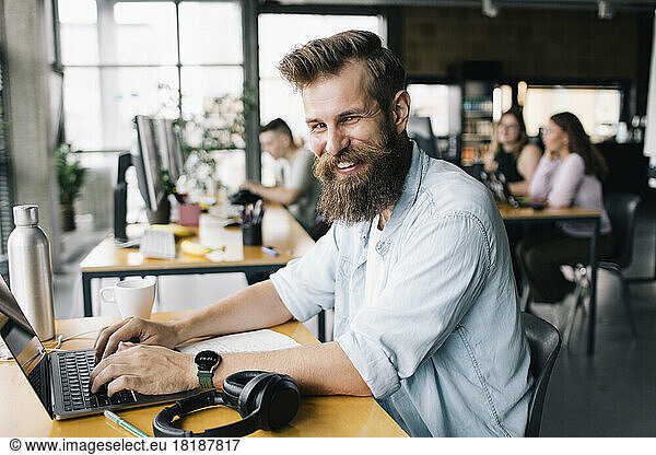 Portrait of smiling male computer programmer typing on laptop while working in office