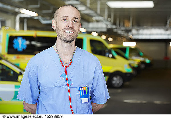 Portrait of smiling male doctor with stethoscope against ambulance in parking lot