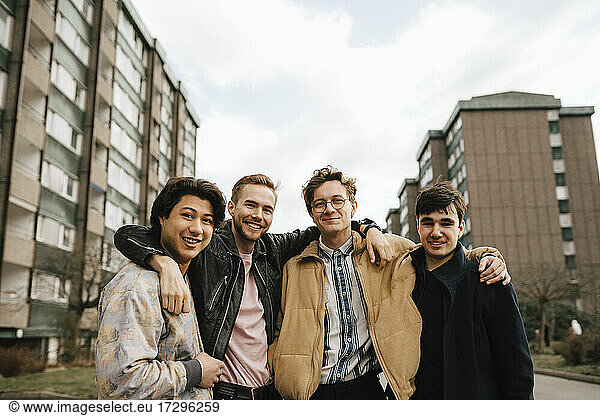 Portrait of smiling male friends with arms around in city