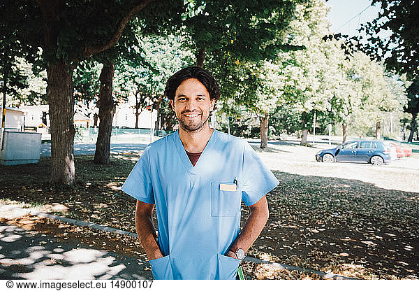 Portrait of smiling male nurse standing with hands in pockets at nursing home