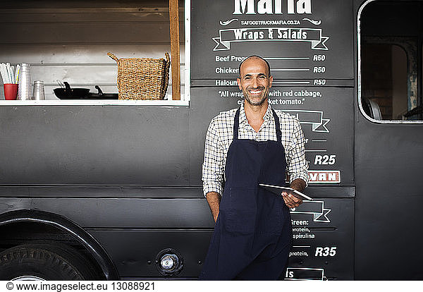Portrait of smiling male owner holding tablet computer while standing against food truck