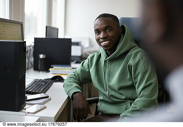 Portrait of smiling male trainee sitting at desk in office