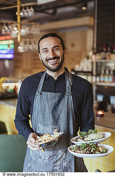 Portrait of smiling male waiter with food in restaurant