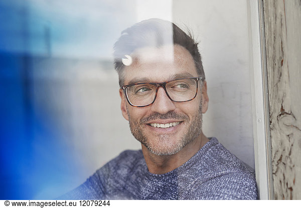 Portrait of smiling man behind glass pane wearing glasses