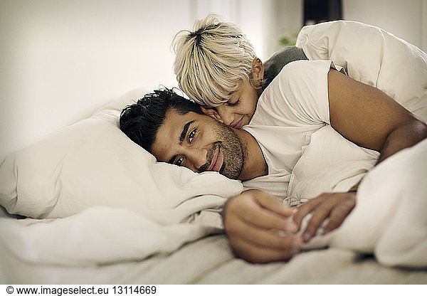 Portrait of smiling man lying with loving woman in bed at home