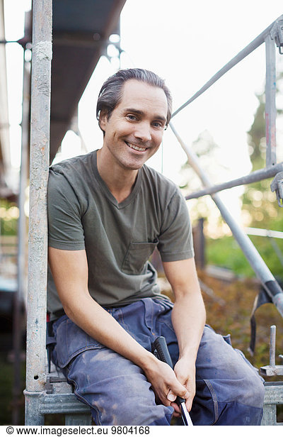 Portrait of smiling man sitting on scaffolding