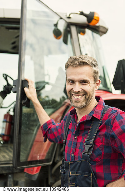Portrait of smiling man standing by tractor at farm