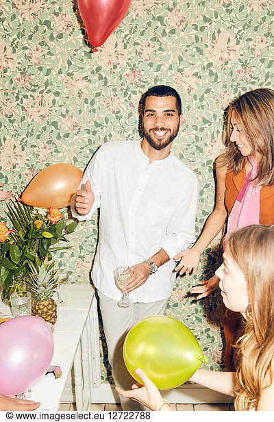 Portrait of smiling man standing with female friends and balloons at home during party