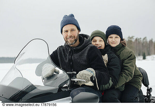 Portrait of smiling man traveling with boys on snowmobile during winter