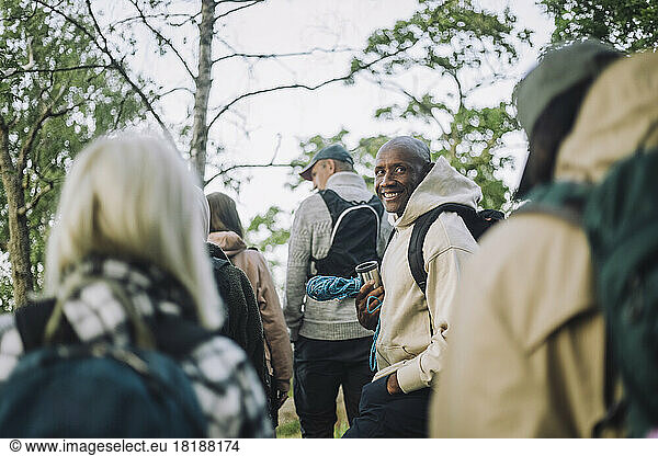 Portrait of smiling man wearing hooded shirt while hiking with friends in forest