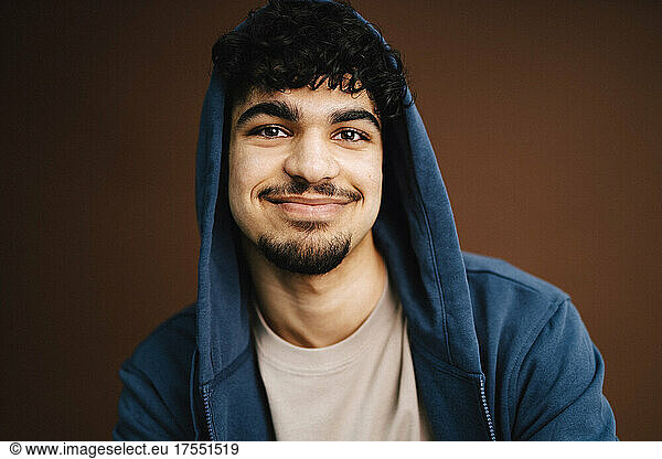 Portrait of smiling man wearing jacket against brown background