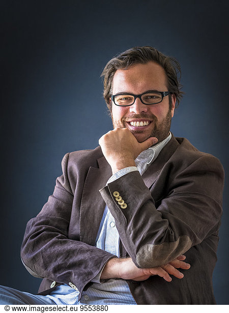 Portrait of smiling man with full beard wearing glasses in front of dark background