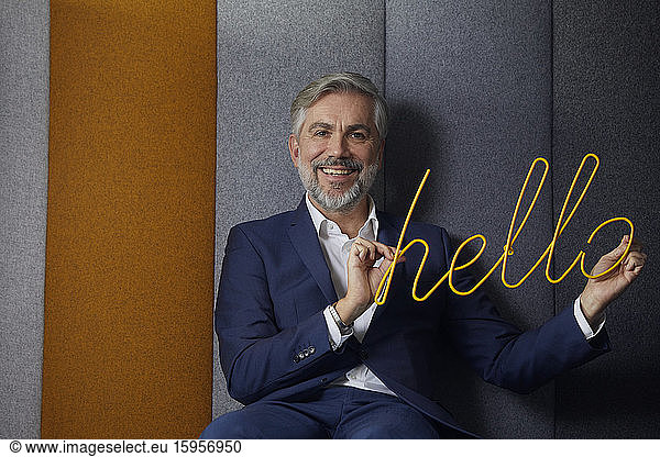Portrait of smiling mature businessman sitting on couch in office holding hello sign