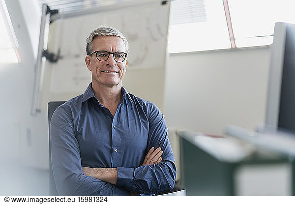 Portrait of smiling mature businessman sitting with arms crossed at desk in office
