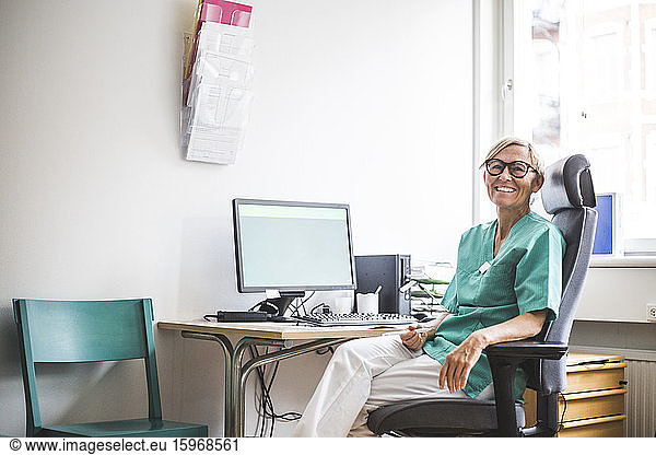 Portrait of smiling mature female doctor sitting on chair at clinic desk