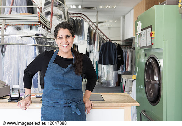 Portrait of smiling mature female dry cleaner standing at Laundromat