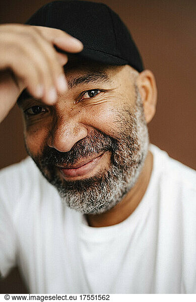 Portrait of smiling mature man holding cap in studio