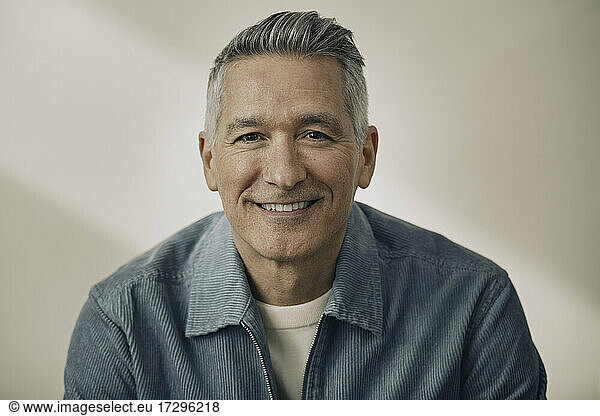 Portrait of smiling mature man wearing blue jacket against beige wall
