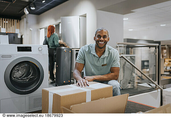 Portrait of smiling mature salesman with cardboard box in appliances store