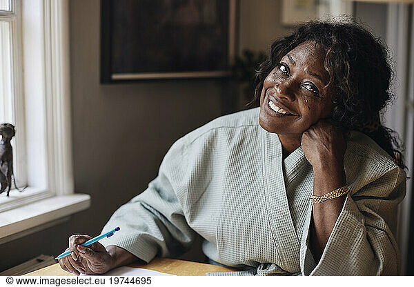 Portrait of smiling mature woman in bathrobe holding pen at home