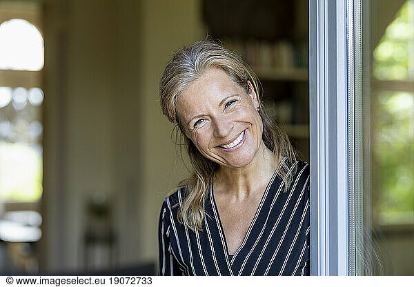 Portrait of smiling mature woman standing at opened terrace door