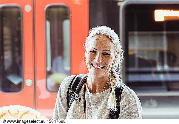 Portrait of smiling mature woman with backpack standing at train station