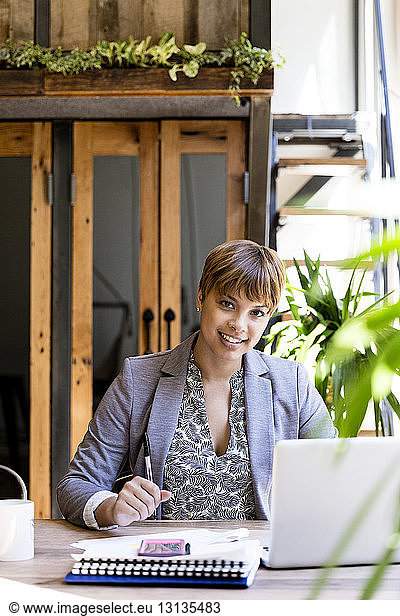 Portrait of smiling mid adult businesswoman using laptop at desk