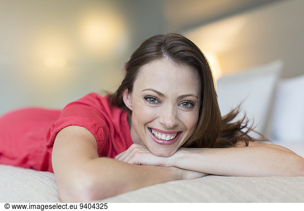 Portrait of smiling mid-adult woman wearing red dress lying on bed in bedroom