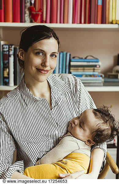 Portrait of smiling mother with sleeping male toddler at home