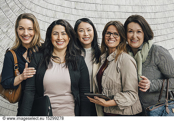 Portrait of smiling multi-ethnic female business professionals standing against wall at workplace