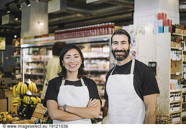 Portrait of smiling multiracial male and female retail clerks wearing aprons standing at grocery store