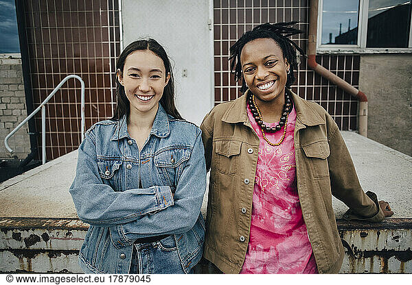 Portrait of smiling multiracial young women standing in front of building