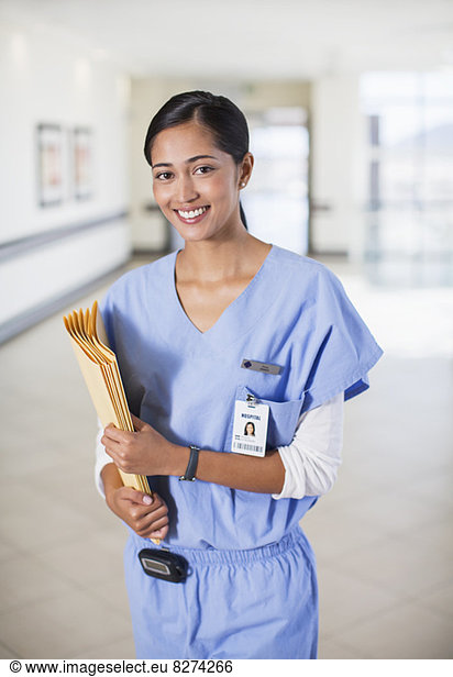 Portrait of smiling nurse with folders in hospital corridor