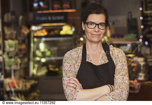 Portrait of smiling owner standing with arms crossed at store
