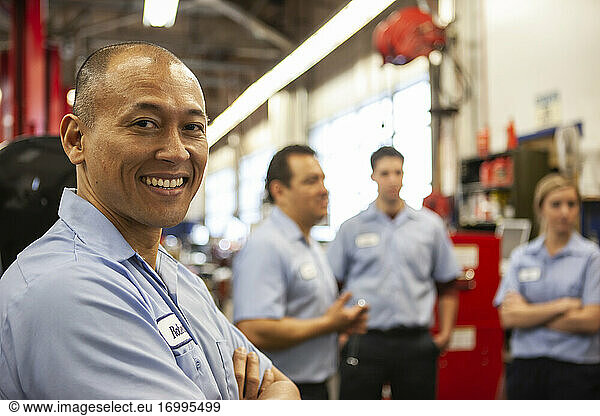 Portrait of smiling Pacific Islander repair shop owner with team in the background