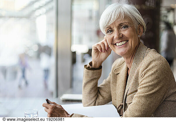 Portrait of smiling senior businesswoman with notebook in a cafe