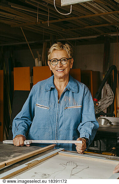 Portrait of smiling senior craftswoman with measuring tape at workshop