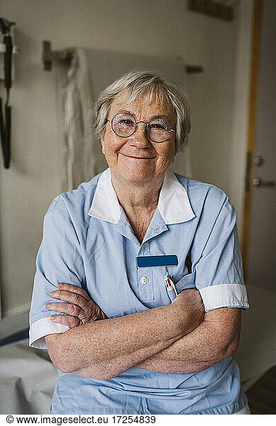 Portrait of smiling senior female doctor standing with arms crossed