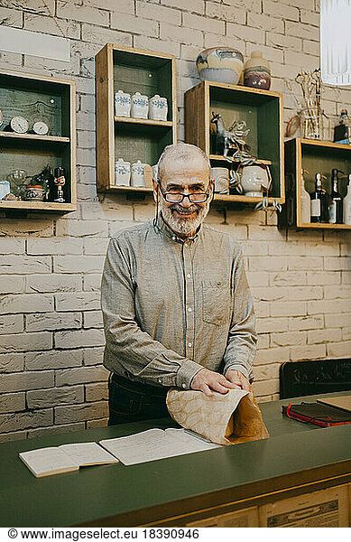 Portrait of smiling senior male owner wrapping box at home decor store