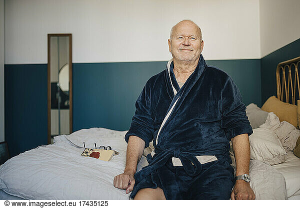 Portrait of smiling senior man in bathrobe on bed at home