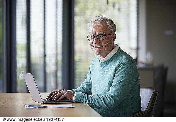 Portrait of smiling senior man using laptop at table at home