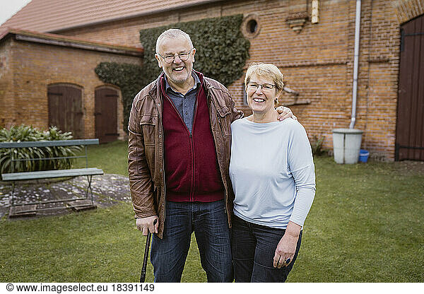 Portrait of smiling senior man with arm around woman standing against house at back yard