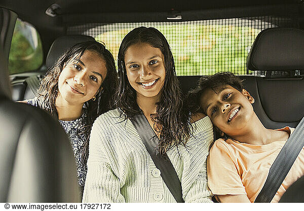 Portrait of smiling siblings wearing seat belt while sitting together on back seat in car