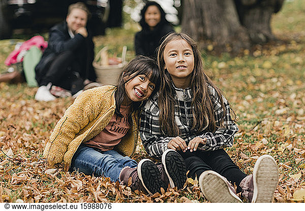 Portrait of smiling sisters sitting on autumn leaves during picnic with parents